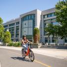 Image of student wearing a helmet, riding an electric bicycle in front of the UC Davis Library.