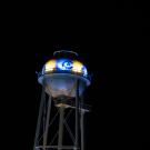 Blue and yellow LEDS shine on a water tower, illuminating the UC Davis Athletics logo
